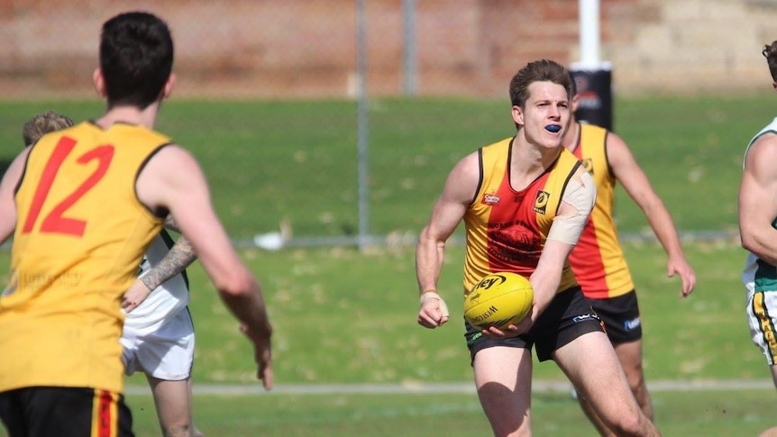 Football player handballs towards a teammate, with players from both teams around him.