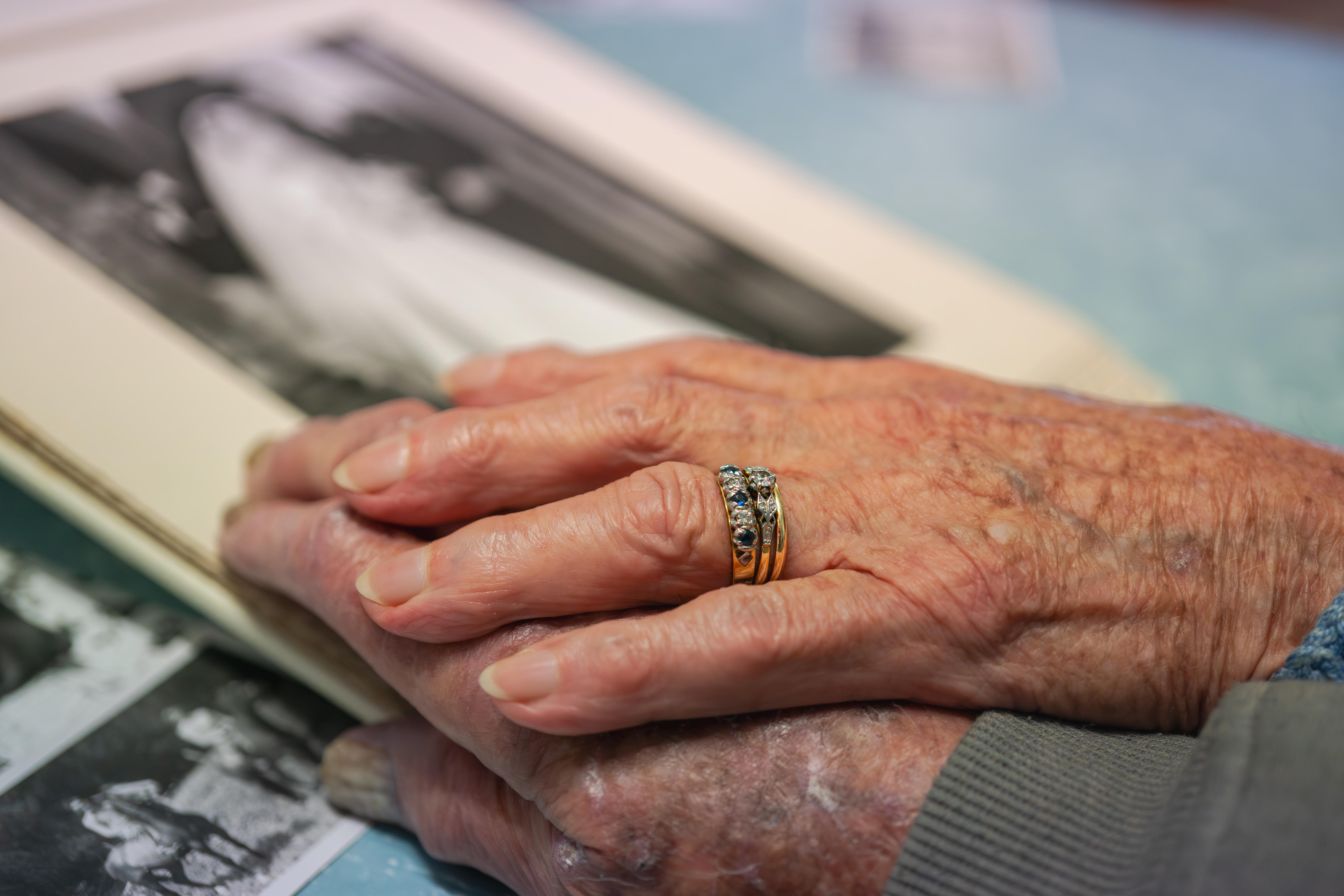 A woman's hand placed on another hand, a wedding ring can be seen. 