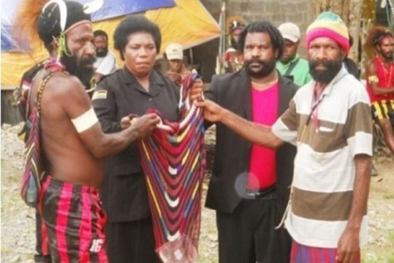 Three Papuan men and a woman hold a woven bag.