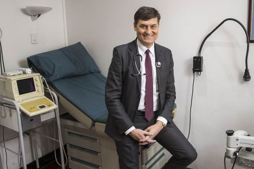 El Dr. Gino Pecoraro se sienta al final de una cama en su oficina.
