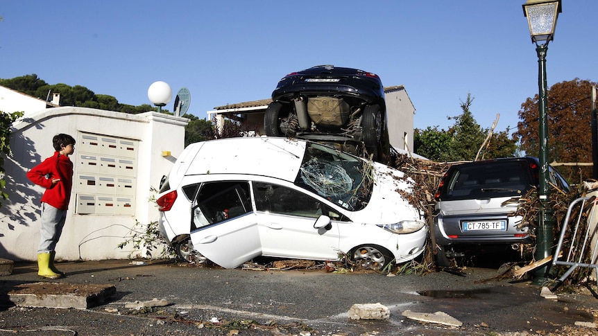 A boy stands next to rubble and damaged cars after violent storms and floods in southeastern France