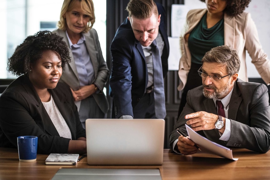 Five people in business attire gathered around a laptop