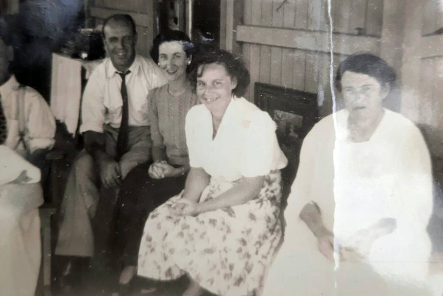 Old black and white photograph of three women and one man sitting on a bench and smiling for a picture 