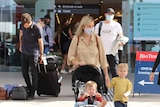 Passengers with bags and face masks, including a woman with two small children, walk out of the exit at Perth Airport.
