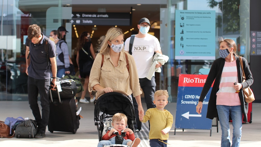 Passengers with bags and face masks, including a woman with two small children, walk out of the exit at Perth Airport.