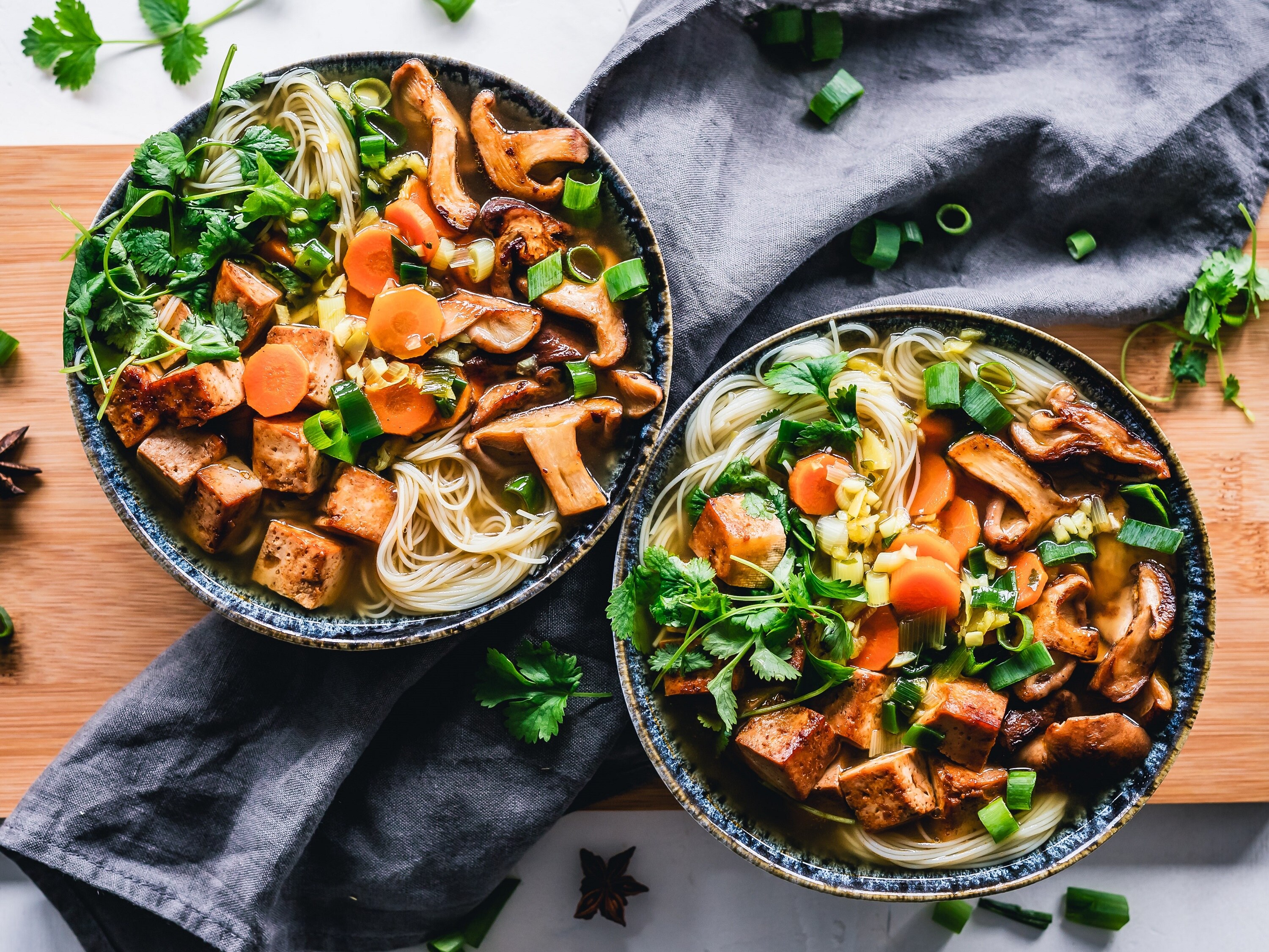 Two bowls of soup with noodles, mushrooms, tofu and carrots and sprinkled with coriander