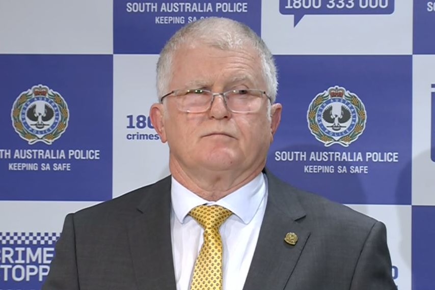 A man in a suit in front of a police sign