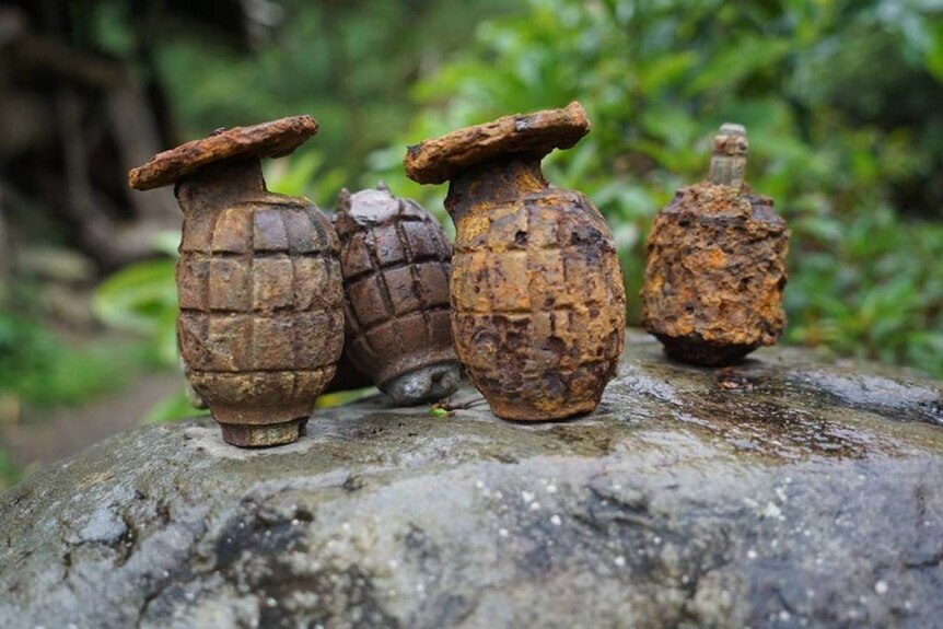 Four rusted grenades on a rock