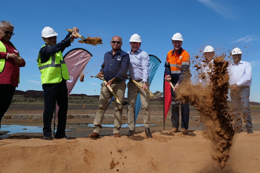 Seven people stand with shovels at a sod turning in a large area of dirt.