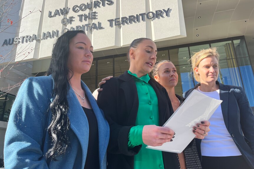 Four women standing outside the ACT Supreme Court. The woman second from the left reads a statement.