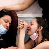 Three women hugging and crying in face masks.
