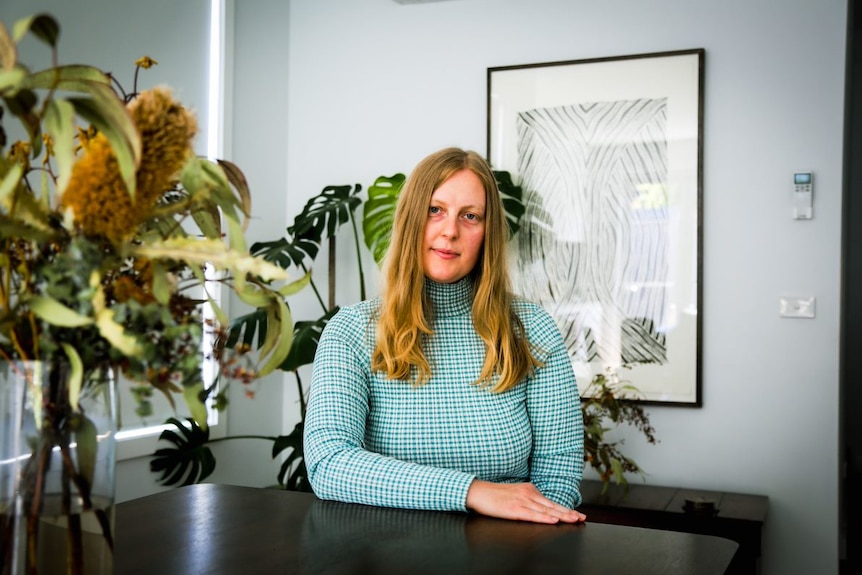 Julia sits at a table next to a vase of flowers and looks at the camera 