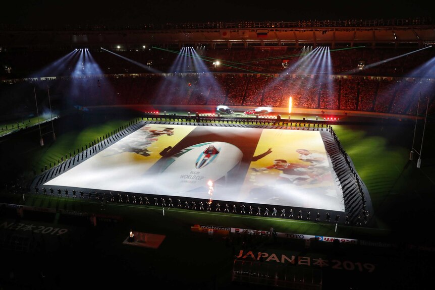 A wide view of performers on a playing field in Tokyo at the Rugby World Cup opening ceremony.