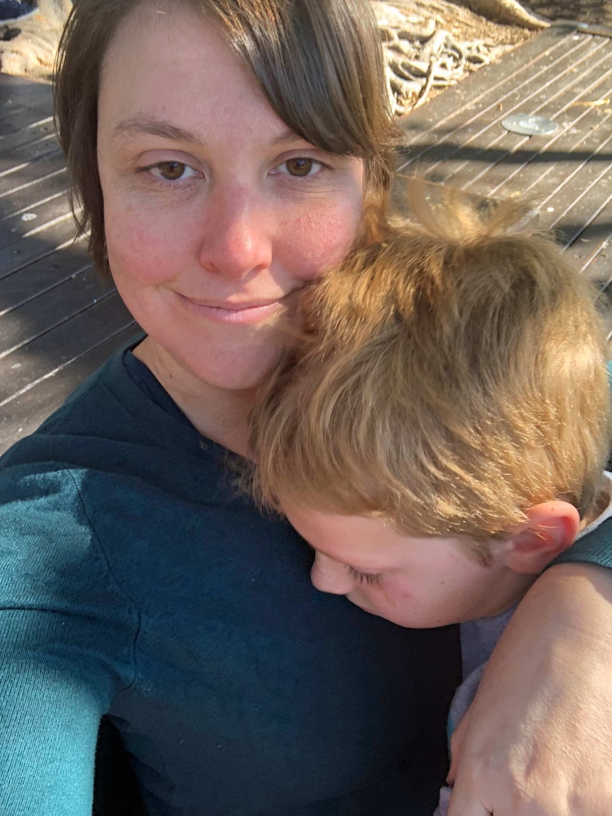 A woman stares into the camera, holding a tired, young boy.