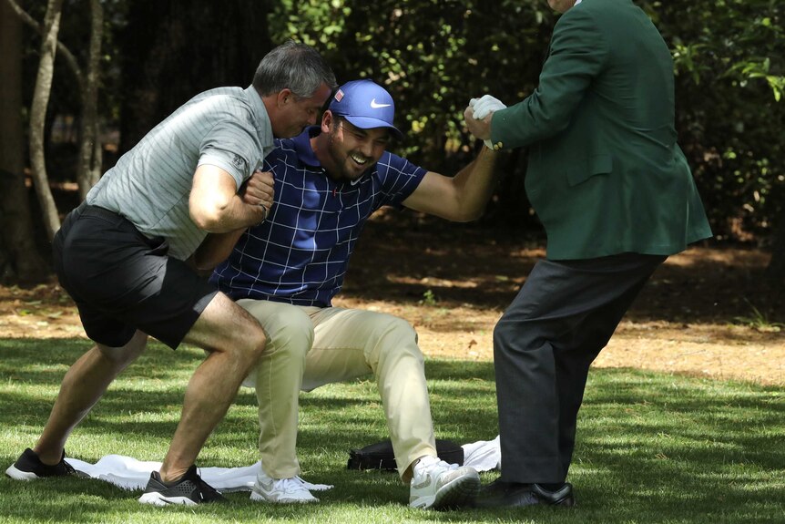 Jason Day is helped off the ground by two men as he grimaces in pain