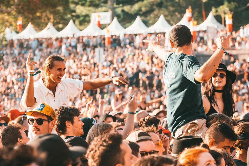 A crowd shot at Splendour In The Grass shows multiple people on the shoulders of others in the afternoon sun.