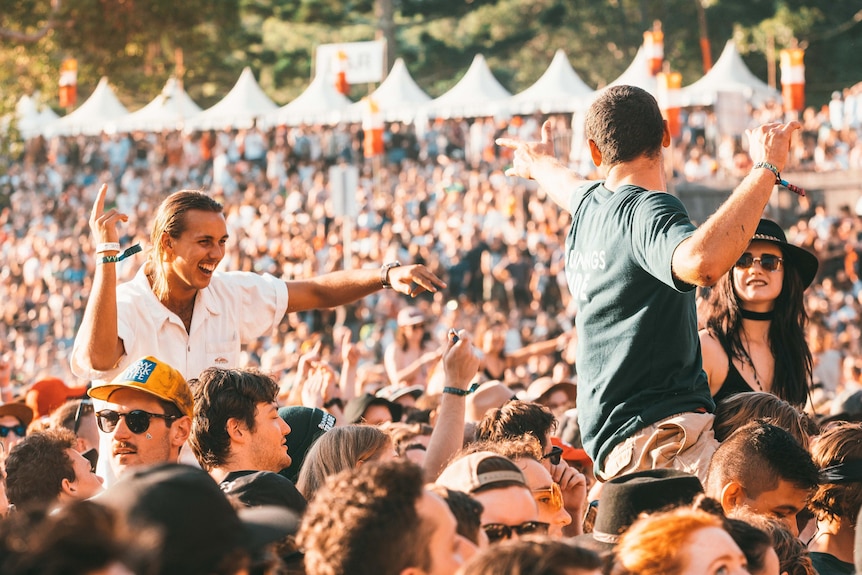 A crowd shot at Splendour In The Grass shows multiple people on the shoulders of others in the afternoon sun.