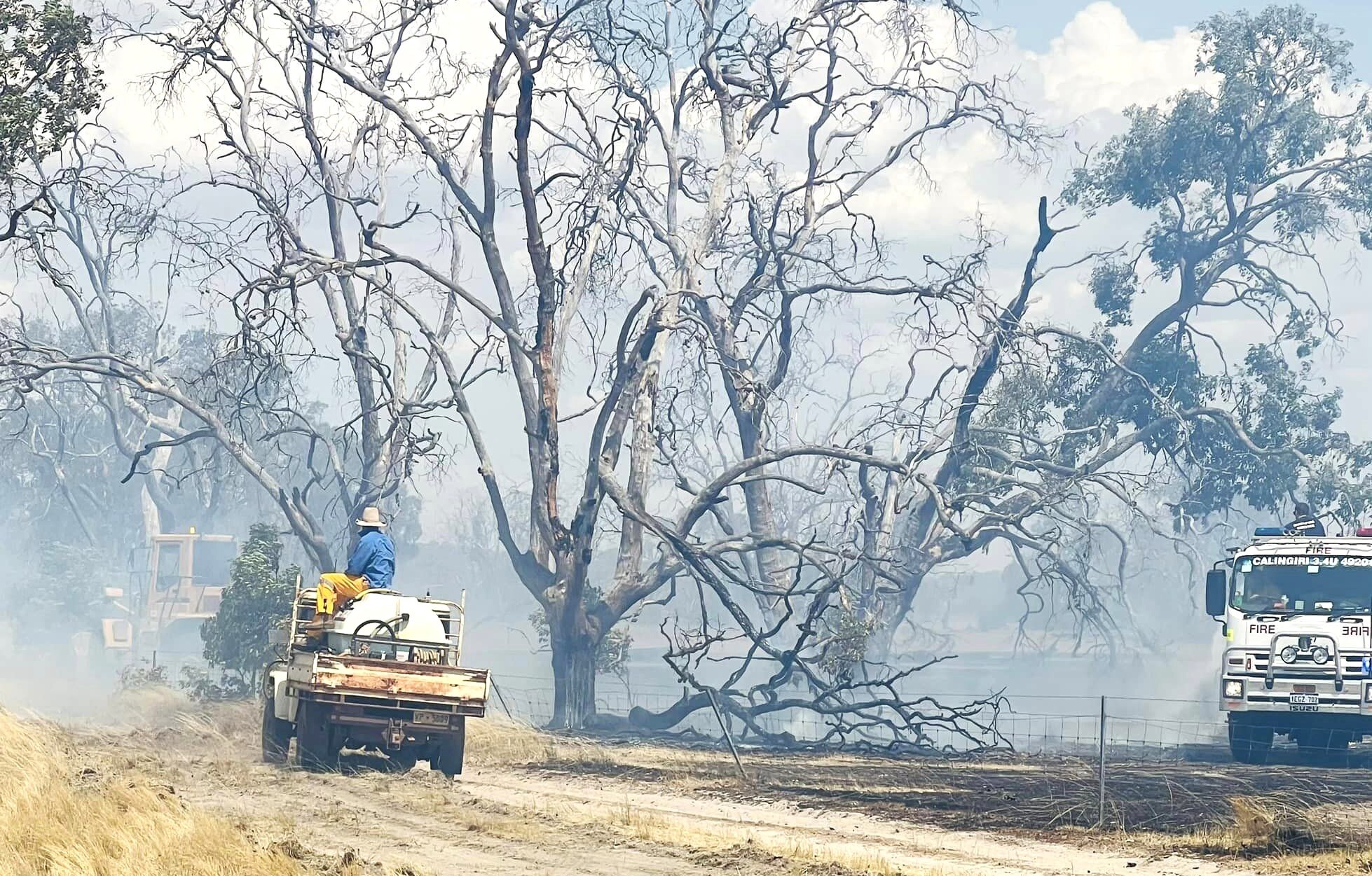 Trucks, utes, and earthmoving equipment fighting a fire.