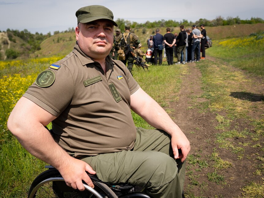 A man in army uniform sits in his wheelchair in a field, looking proud 