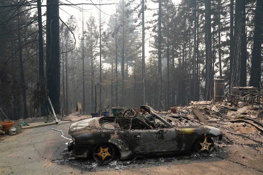 A charred vehicle is parked in front of a damaged home in Bonny Doon, California.