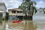 A boy sits in a canoe down a flooded street.