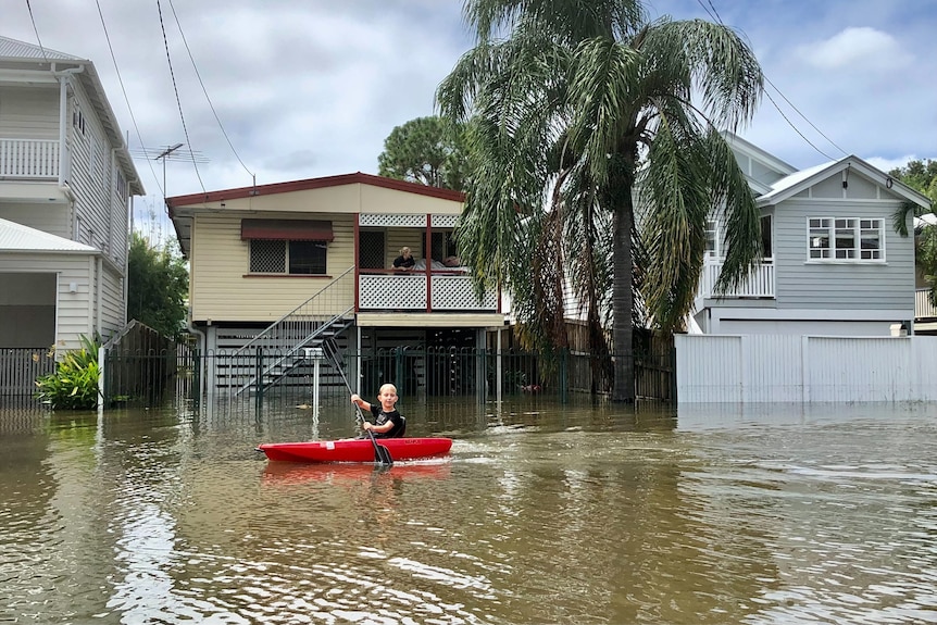 A boy sits in a canoe down a flooded street.