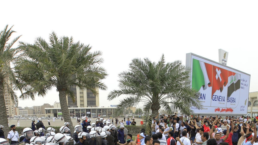 Anti-government protesters shout slogans at riot policemen as they block a road in Manama