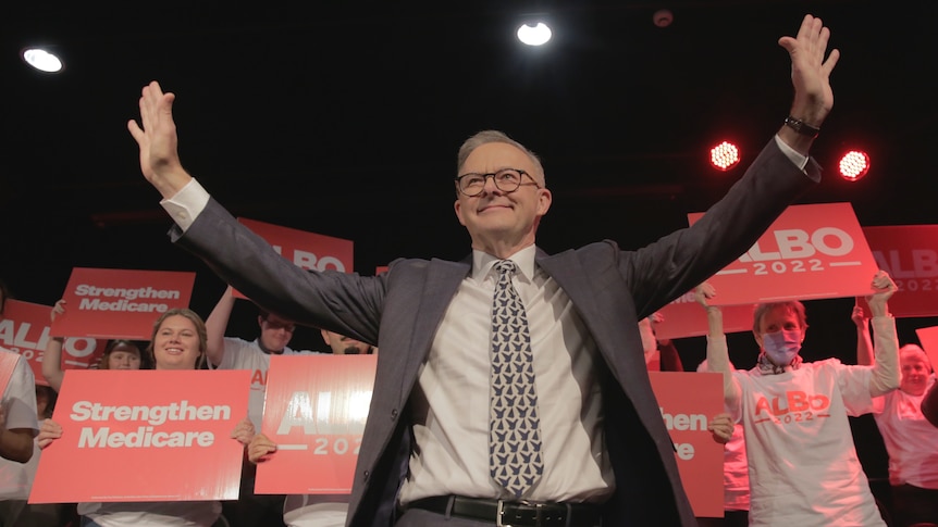 Anthony Albanese has his hands in the air in front of Labor and Albo signs 