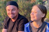 Leonardo DiCaprio and Greta Thunberg smile together while sitting outside among greenery.