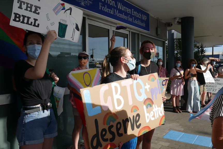 People holding placards and protesting with LGBT flags.