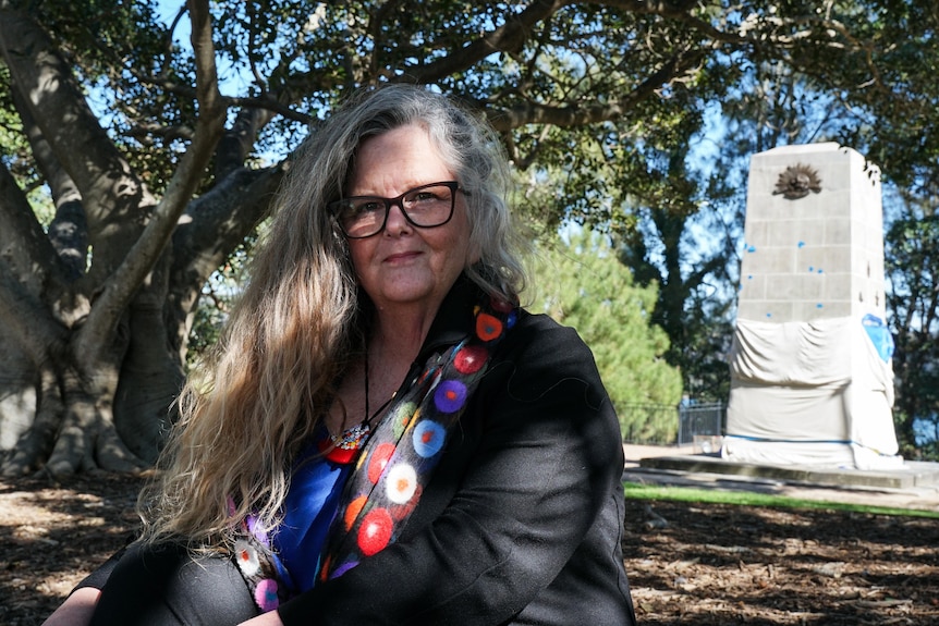 Lady with lonh wavy hair, colourful scarf and glasses with cenotaph in the background