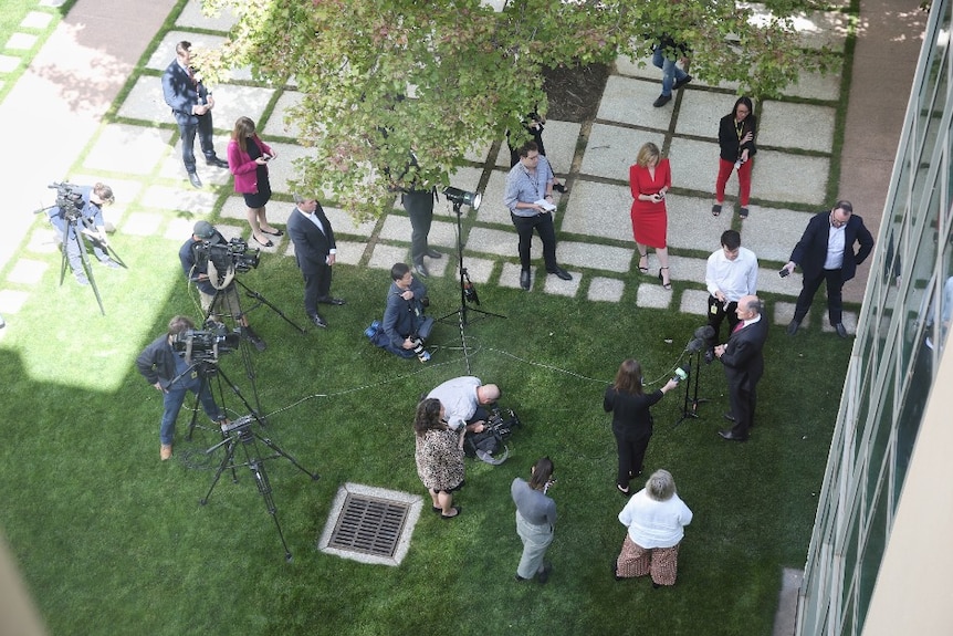 Aerial shot of journalists and camera crews dotted around courtyard as minister stands in front of microphones.