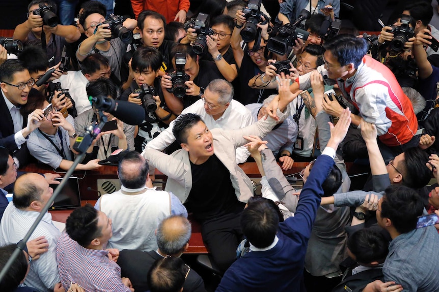 Law-makers fighting are tightly surrounded by dozens of reporters and photographers in a chaotic scene