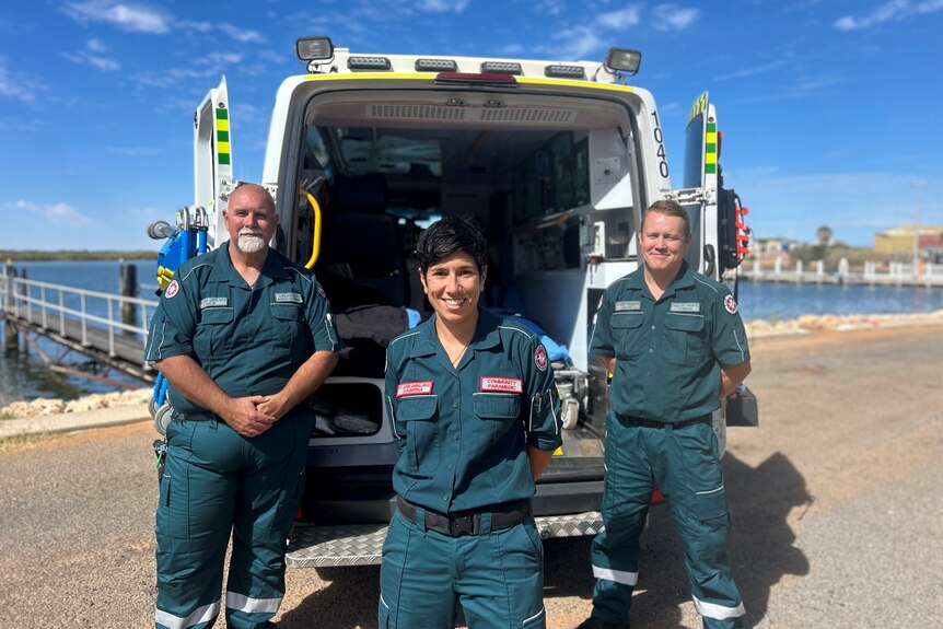 Two men and a woman standing in front of an ambulance