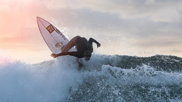 A female surfer carves a wave at sunset.