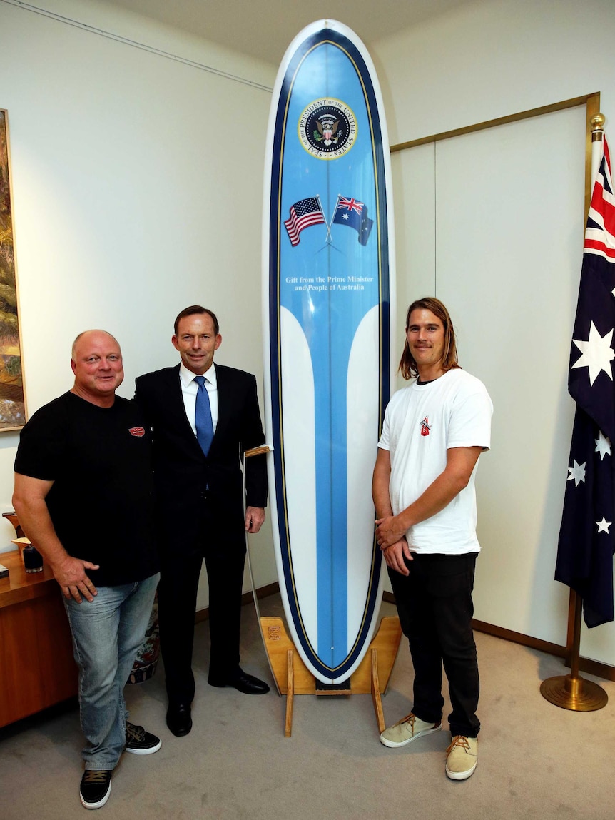 Prime Minister Tony Abbott stands with a surfboard he will present to President Barack Obama.