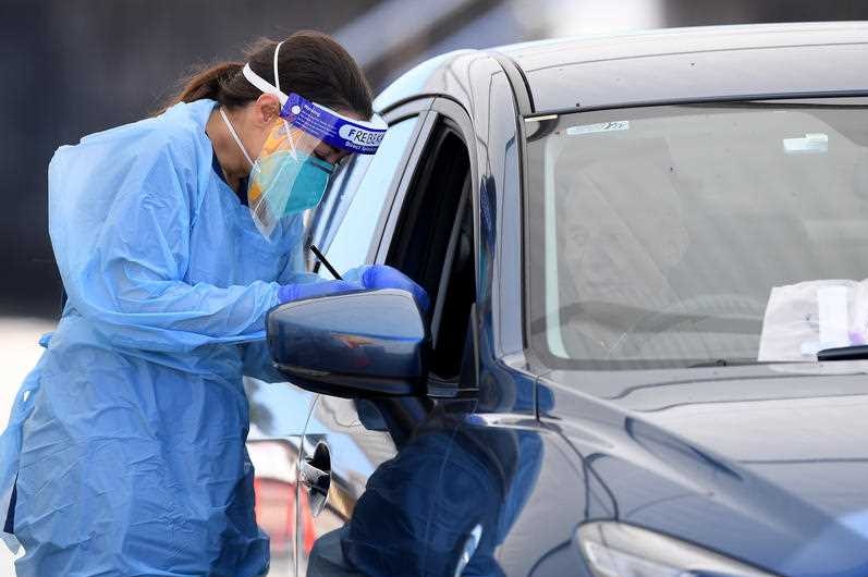 A nurse in protective gear testing a person in a car.