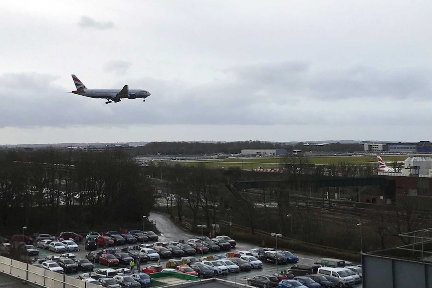 A plane flying over the Gatwick airport and a carpark.