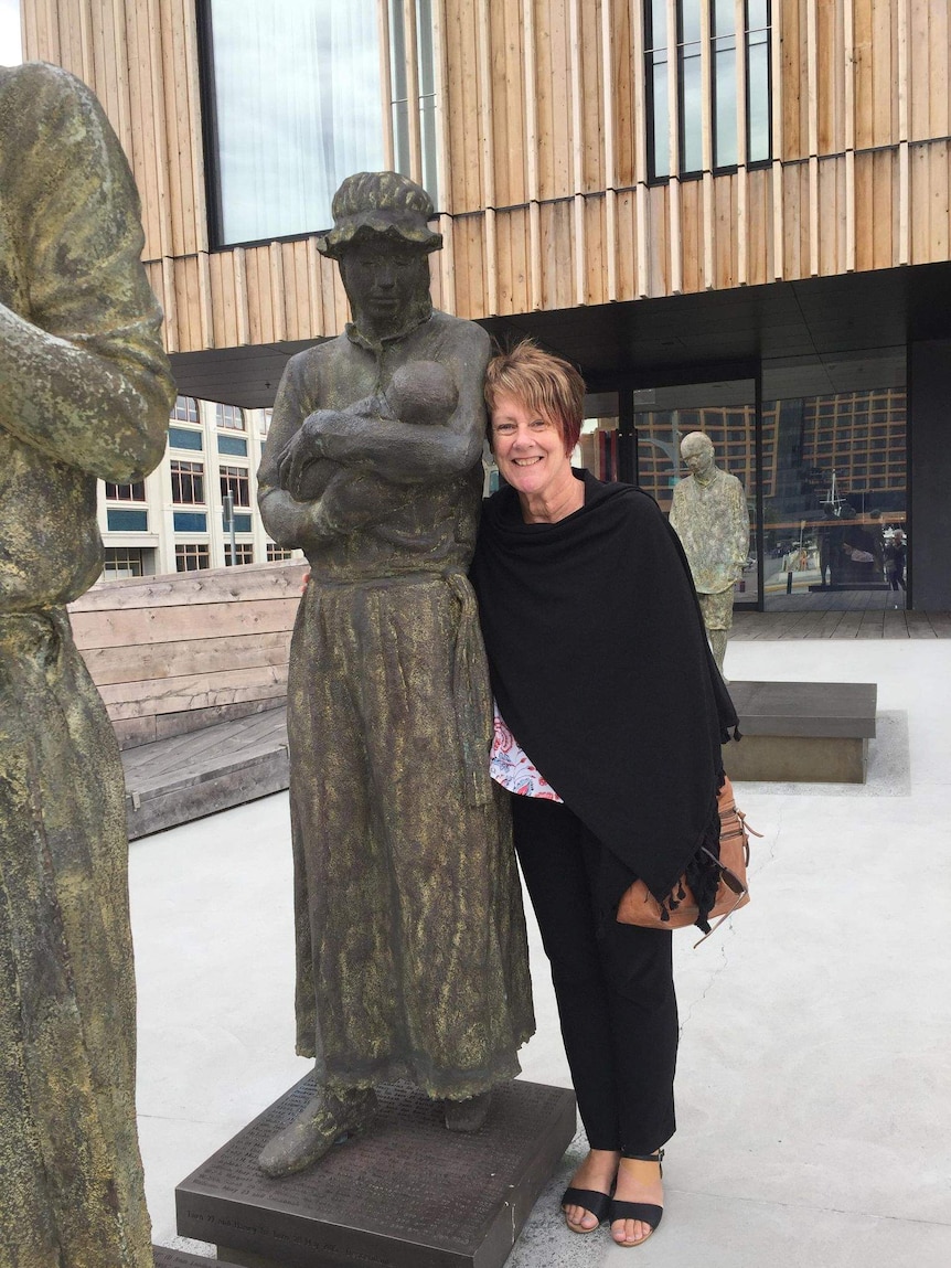 A woman huddles against a bronze statue of mother and child