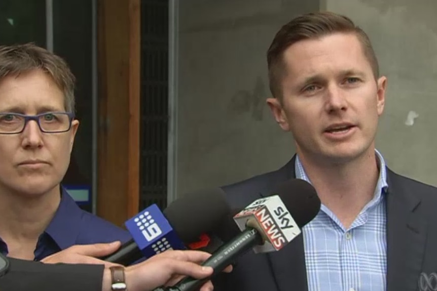 Daniel Walton Australian Workers Union, wears a suit, blue checked shirt, open collar, speak into Sky News, Nine microphones.