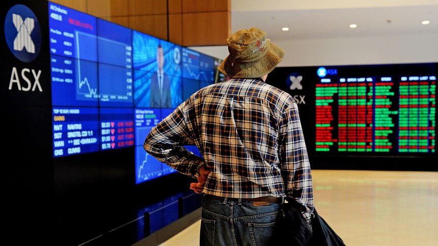 An elderly man watches a share market prices display.