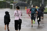 A man and two boys run in the rain at South Bank while a woman walks with an umbrella.