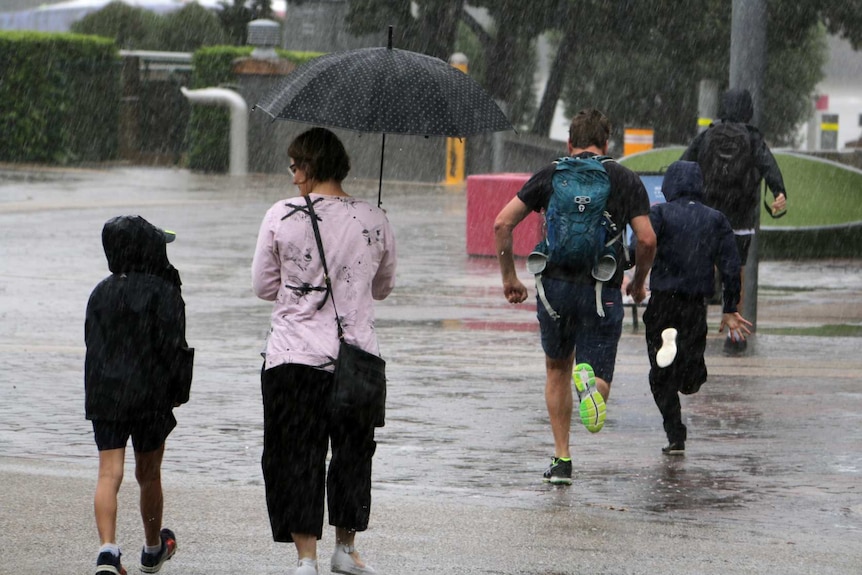 A man and two boys run in the rain at South Bank while a woman walks with an umbrella.