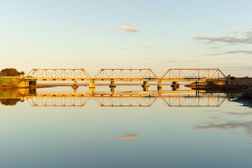 a metal bridge spanning across a very still and calm river