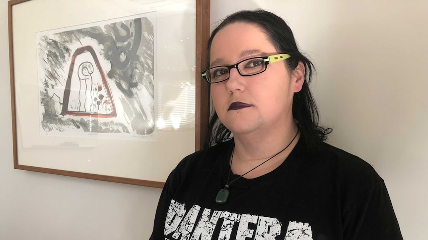 Woman with black hair, black lipstick and band t-shirt looks at camera.