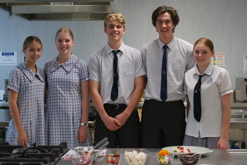 A group of year 10 students stands in a school home economics kitchen, smiling.