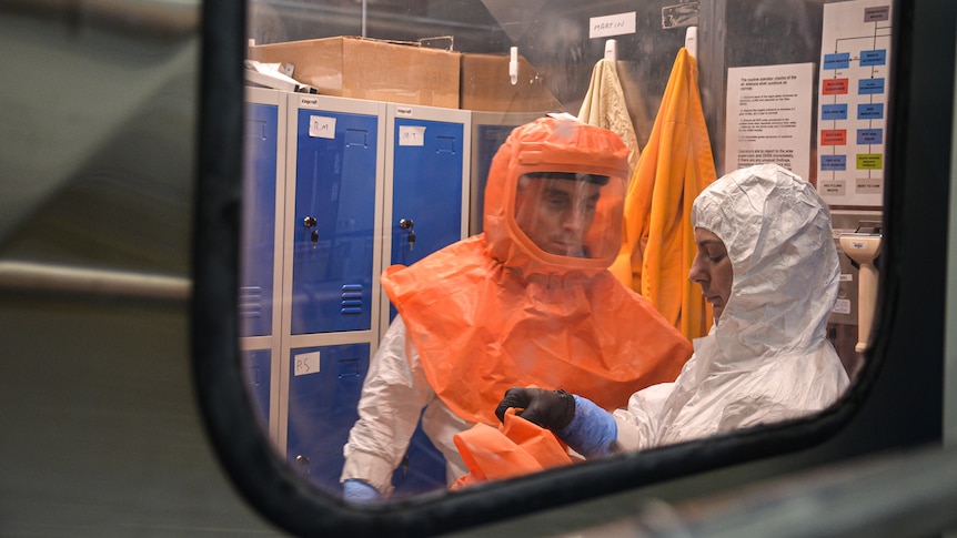One of the workers is seen with an orange hood and visor on, while the other is in a white protective suit