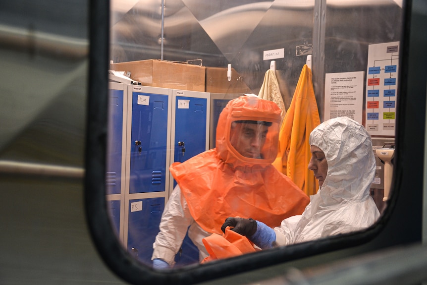 One of the workers is seen with an orange hood and visor on, while the other is in a white protective suit