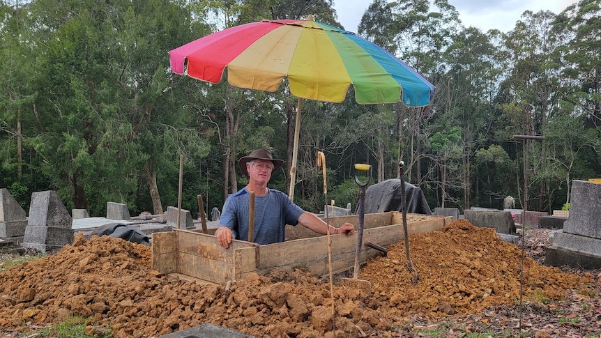A man standing in a grave site with a bright umbrella over him 