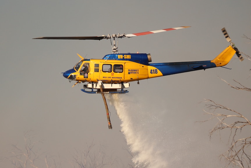 A helicopter dumps water on a fire behind a house.